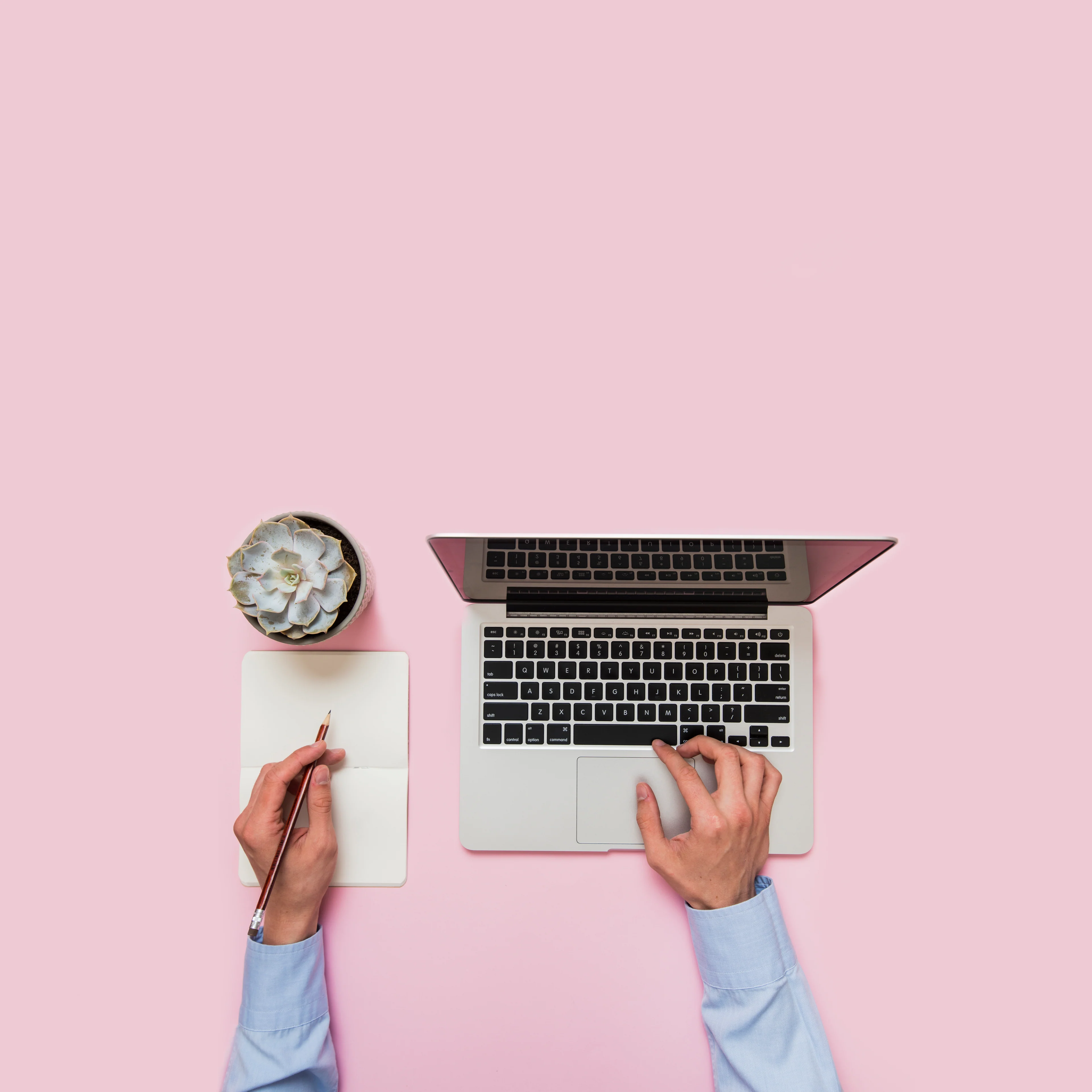 Un espacio de trabajo con computadora y libreta sobre una mesa rosa
